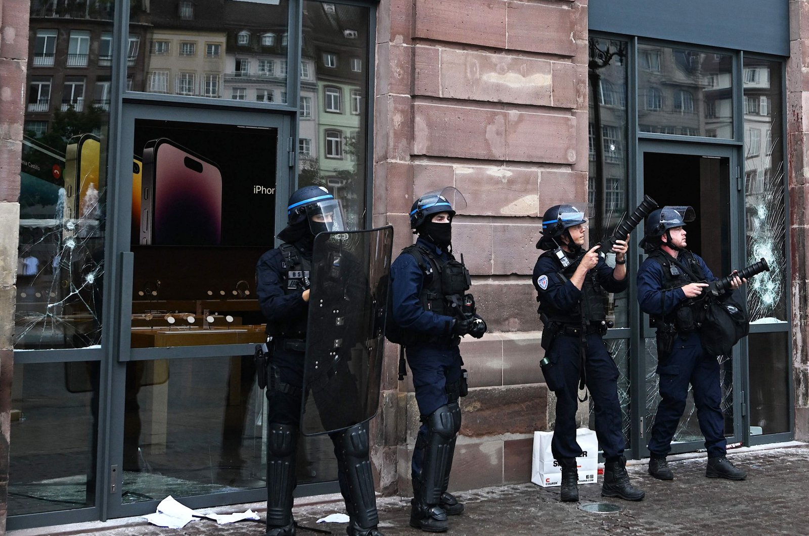 French police officers in riot gear stand guard and hold tear gas canister launchers next to the facade of a damaged Apple Store at Place Kleber, in Strasbourg, eastern France, on June 30, 2023. (AFP Photo)