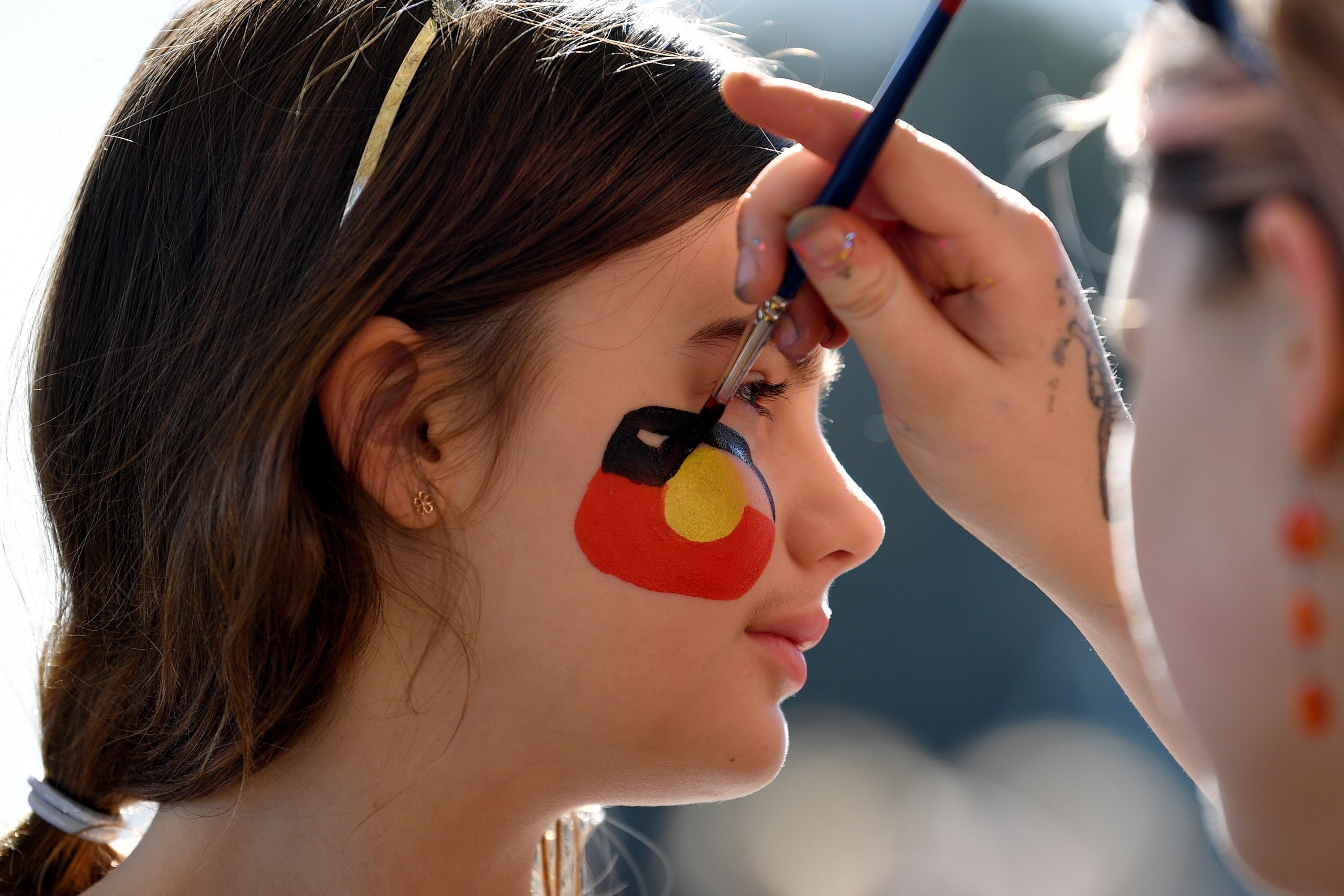 Seorang gadis melukis bendera Aborigin di wajahnya selama acara komunitas 'Yes23' untuk mendukung Suara Pribumi ke Parlemen, di Sydney, Australia, 2 Juli 2023. (Foto EPA)