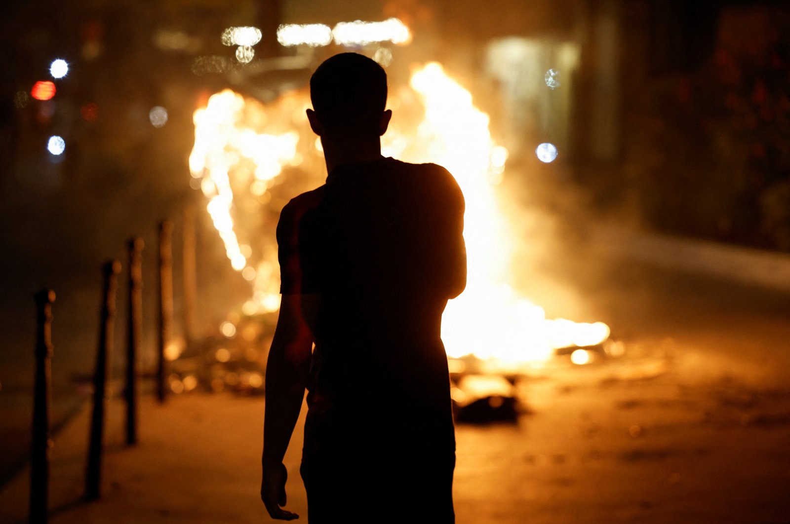 A person stands near a burning container as people protest following the death of Nahel, a 17-year-old teenager killed by a French police officer in Nanterre during a traffic stop, and against police violence, in Paris, France, June 30, 2023. (Reuters Photo)