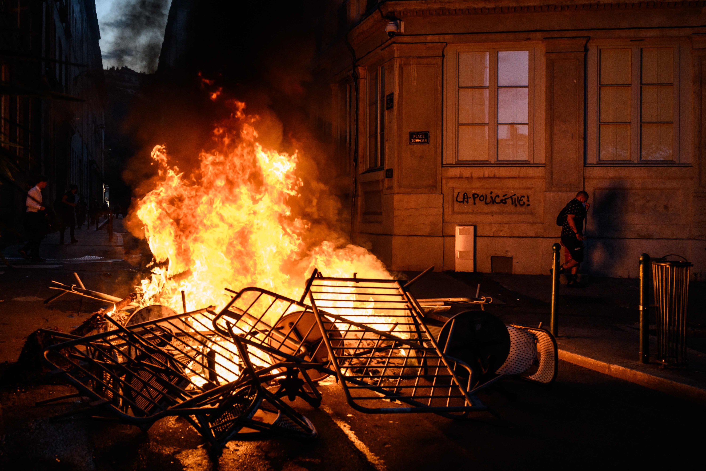 Seorang wanita berjalan melewati api saat terjadi bentrokan dengan polisi di Lyon, Prancis tenggara, 30 Juni 2023. (AFP Photo)