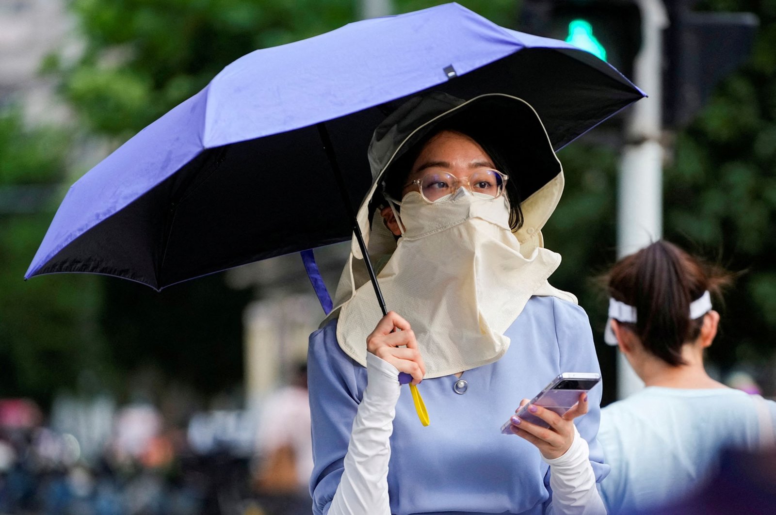 A woman walks on a street as she shields herself from the sun with a hat, mask and umbrella, amid an alert for a heat wave in Shanghai, China, July 4, 2023. (Reuters Photo)