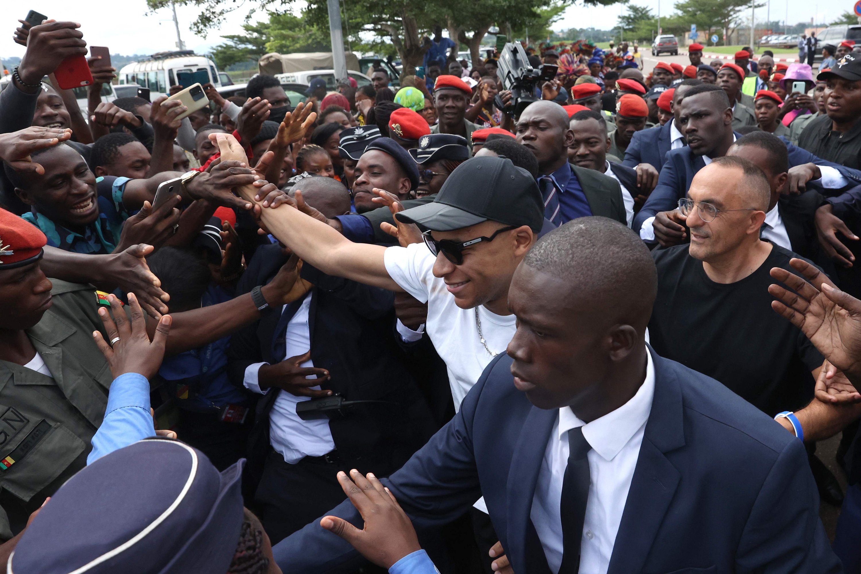 Striker bintang tim sepak bola nasional Paris Saint-Germain dan Prancis Kylian Mbappe (Tengah) menyapa orang banyak yang berkumpul di luar Bandara Yaounde saat ia tiba untuk kunjungan amal dan tur ke desa ayahnya, Yaounde, Kamerun, 6 Juli 2023. (AFP )