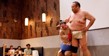 Nadine, a 43-year-old tourist from the U.S., wearing a sumo wrestler costume, tries to spar against former sumo wrestler Towanoyama on the sumo ring before tourists from abroad, Tokyo, Japan, June 30, 2023. (Reuters Photo)