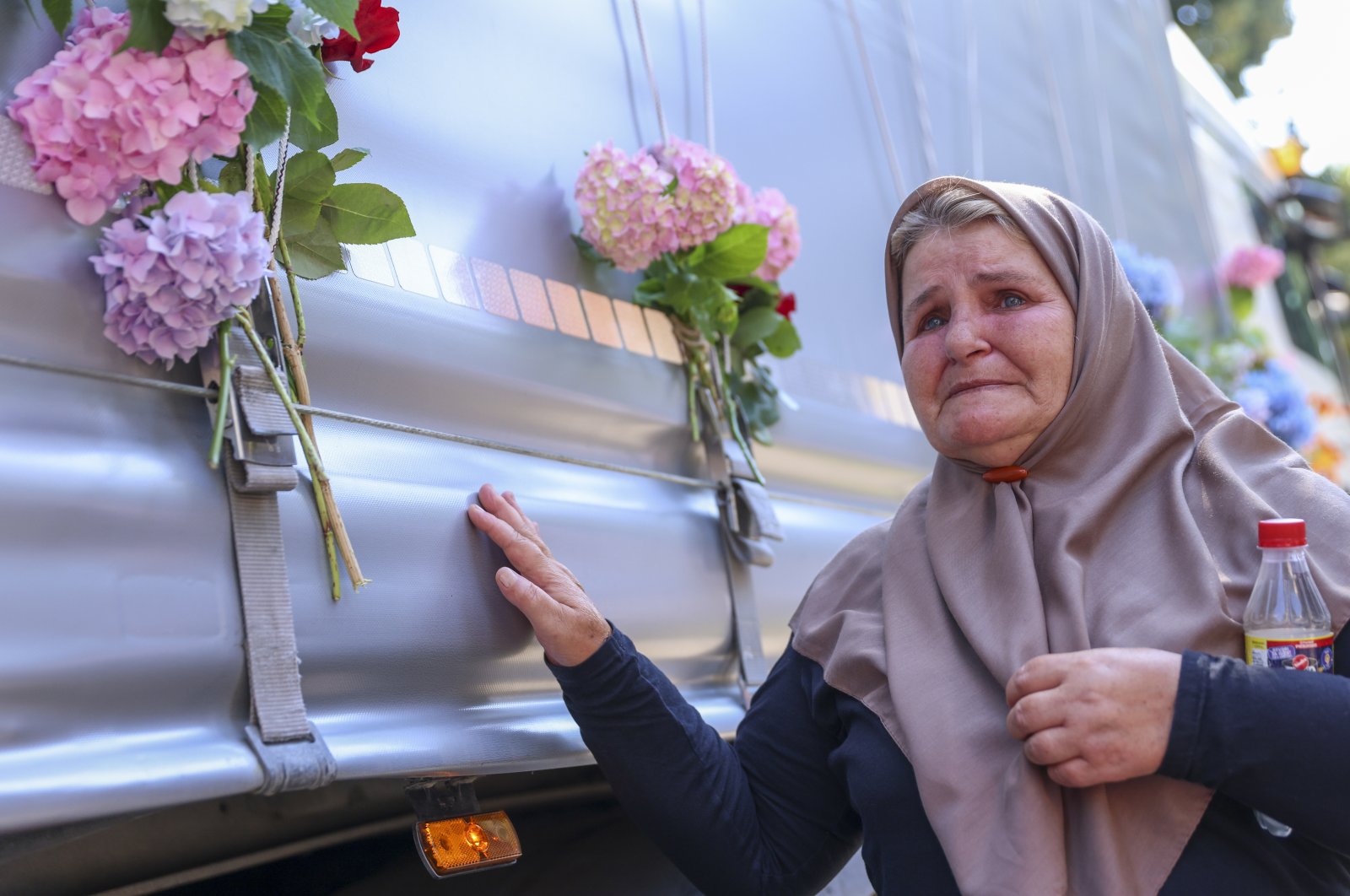 A woman places a flower on a truck carrying 30 coffins with remains of the recently identified victims of the 1995 Srebrenica genocide, in Visoko, Bosnia, July 9, 2023. (AP Photo)