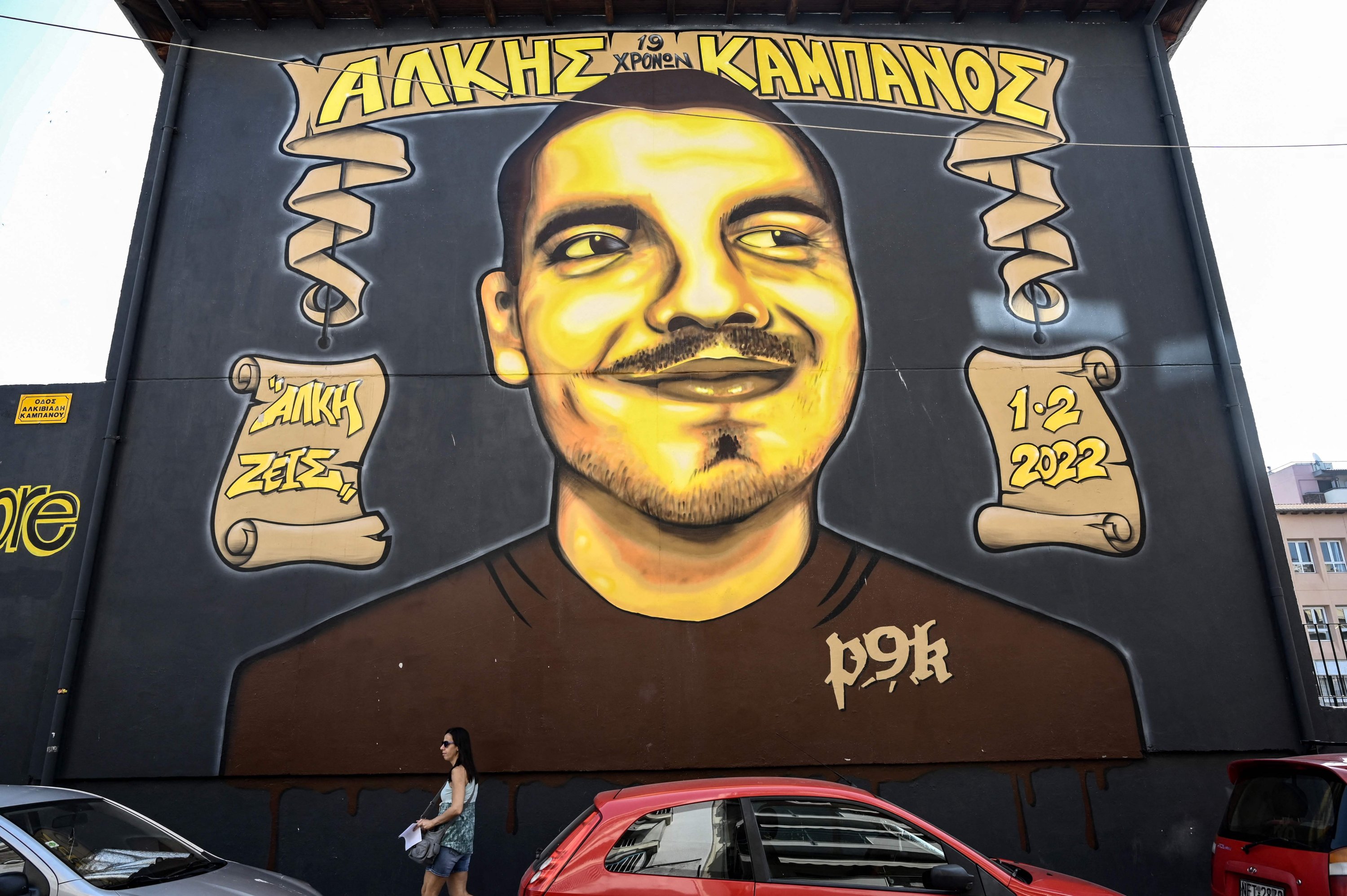 Seorang wanita berjalan melewati mural yang memuat potret mendiang penggemar sepak bola Alkis Kampanos, di dekat tempat dia dibunuh oleh hooligan muda, Thessaloniki, Yunani, 12 Juli 2023. (AFP Photo)