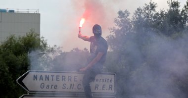 An attendee waves a light flare as he stands atop a street sign during a commemoration march for Nahel, a teenage driver shot dead by police, in the Parisian suburb of Nanterre, France, June 29, 2023. (AFP Photo)