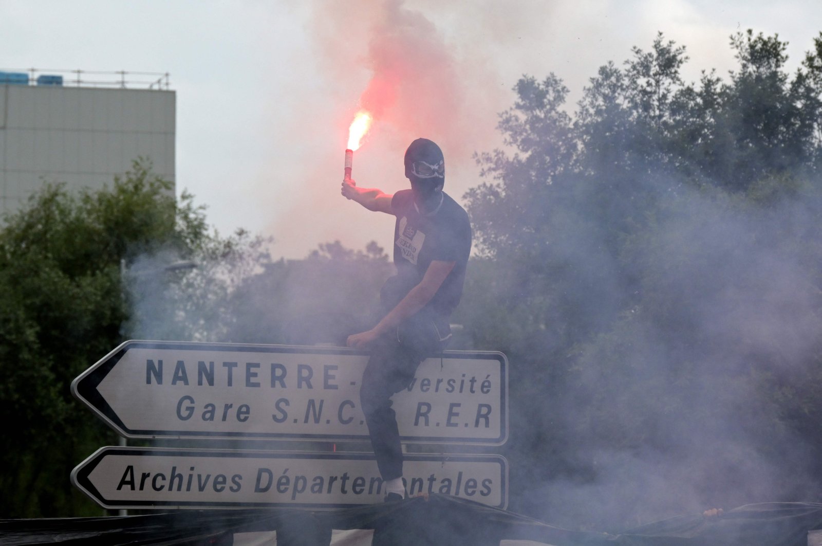 An attendee waves a light flare as he stands atop a street sign during a commemoration march for Nahel, a teenage driver shot dead by police, in the Parisian suburb of Nanterre, France, June 29, 2023. (AFP Photo)