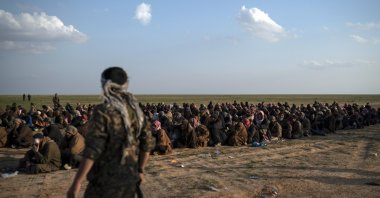 A terrorist PKK/YPG dominated-SDF member stands next to men evacuated out of the last territory held by Daesh, near Baghouz, eastern Syria, Feb. 22, 2019. (AP File Photo)