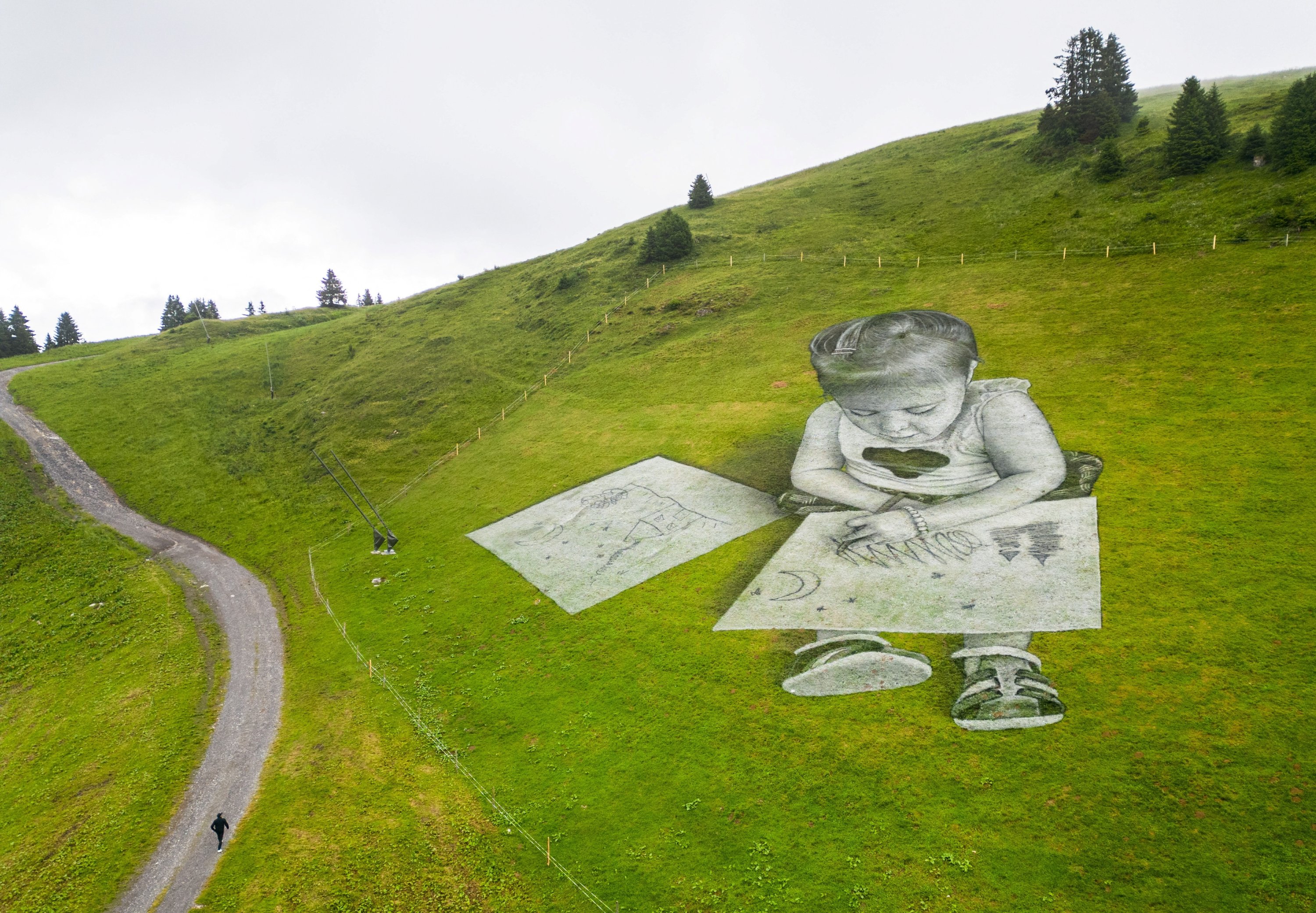Seniman Swiss-Prancis SAYPE berjalan menuju lukisan seni tanahnya yang mewakili gambar seorang anak di Col de Bretaye di Villars-sur-Ollon, Swiss, 13 Juli 2023. (Foto Reuters)