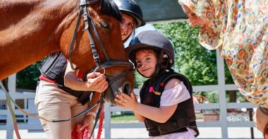A disabled child pets a horse at Türkiye Jockey Club Equine Therapy Center, in Izmir, Türkiye, July 15, 2023. (AA Photo)