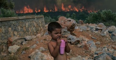 A child reacts as a wildfire burns in the village of Agios Charalabos, near Athens, July 18, 2023. (AFP Photo)