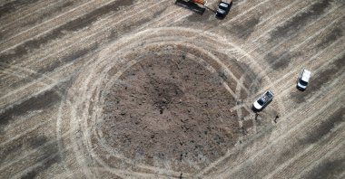 A farmer collects harvest in a field ten kilometers from the front line, around a crater left by a Russian rocket in the foreground, in the Dnipropetrovsk region, Ukraine, on July 4, 2022. (AP File Photo)