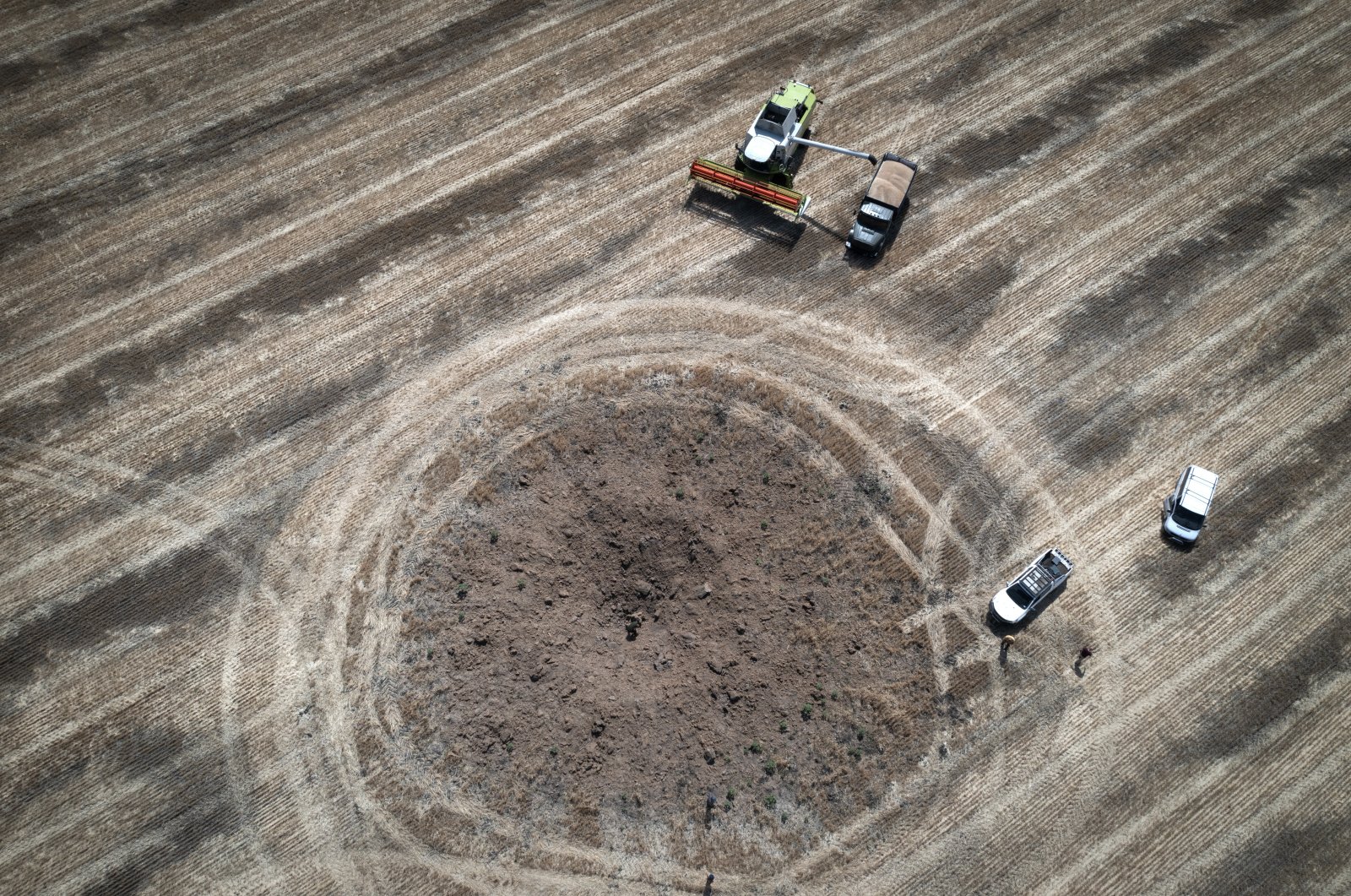A farmer collects harvest in a field ten kilometers from the front line, around a crater left by a Russian rocket in the foreground, in the Dnipropetrovsk region, Ukraine, on July 4, 2022. (AP File Photo)