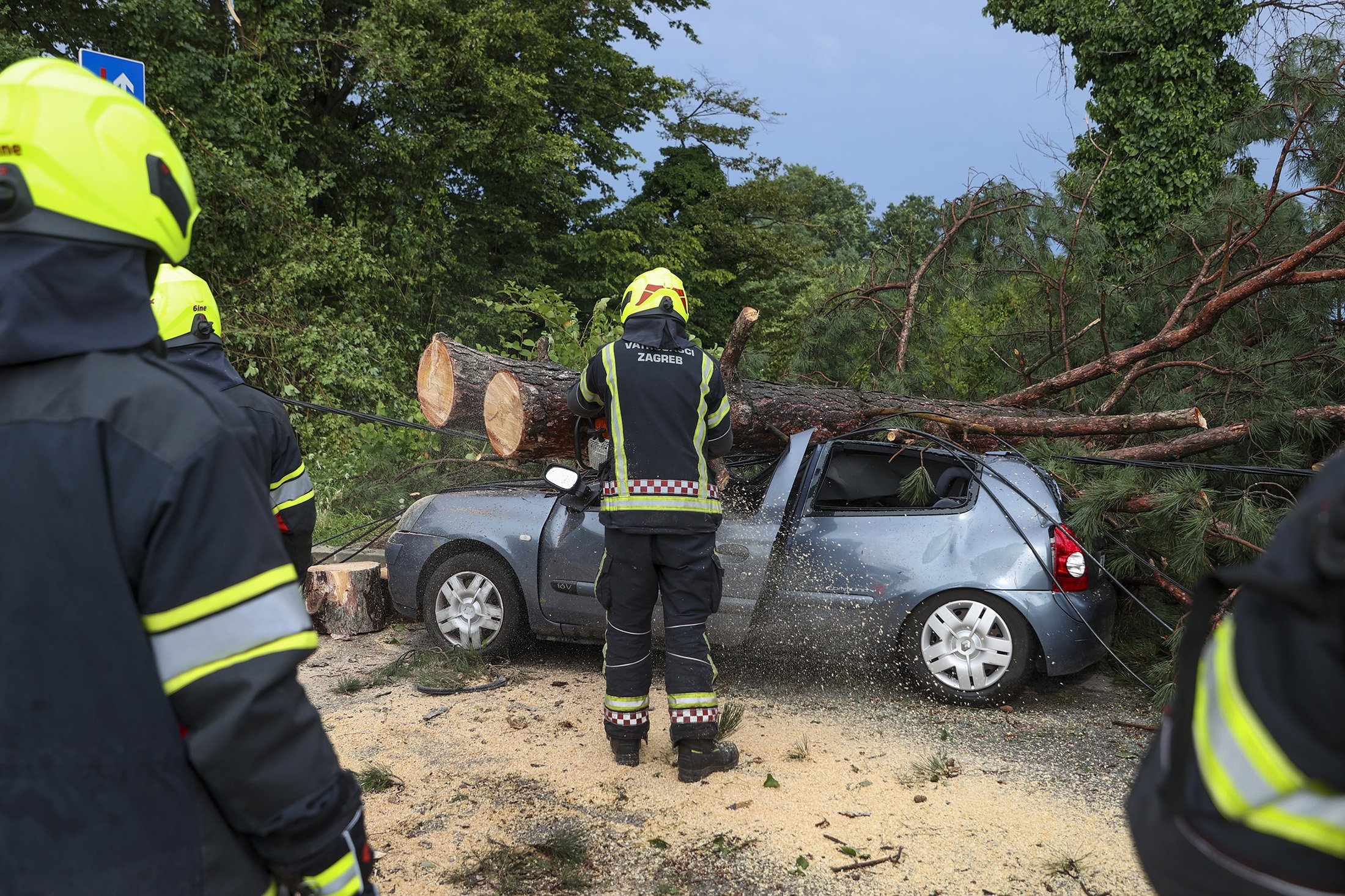 Petugas pemadam kebakaran memindahkan ranting pohon yang tumbang dari mobil yang diparkir rusak setelah badai dahsyat, di Zagreb, Kroasia, 19 Juli 2023. (Foto AP)