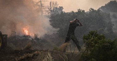 A man reacts as a helicopter sprays water at a fire on the island of Rhodes, Greece, July 25, 2023. (AFP Photo)