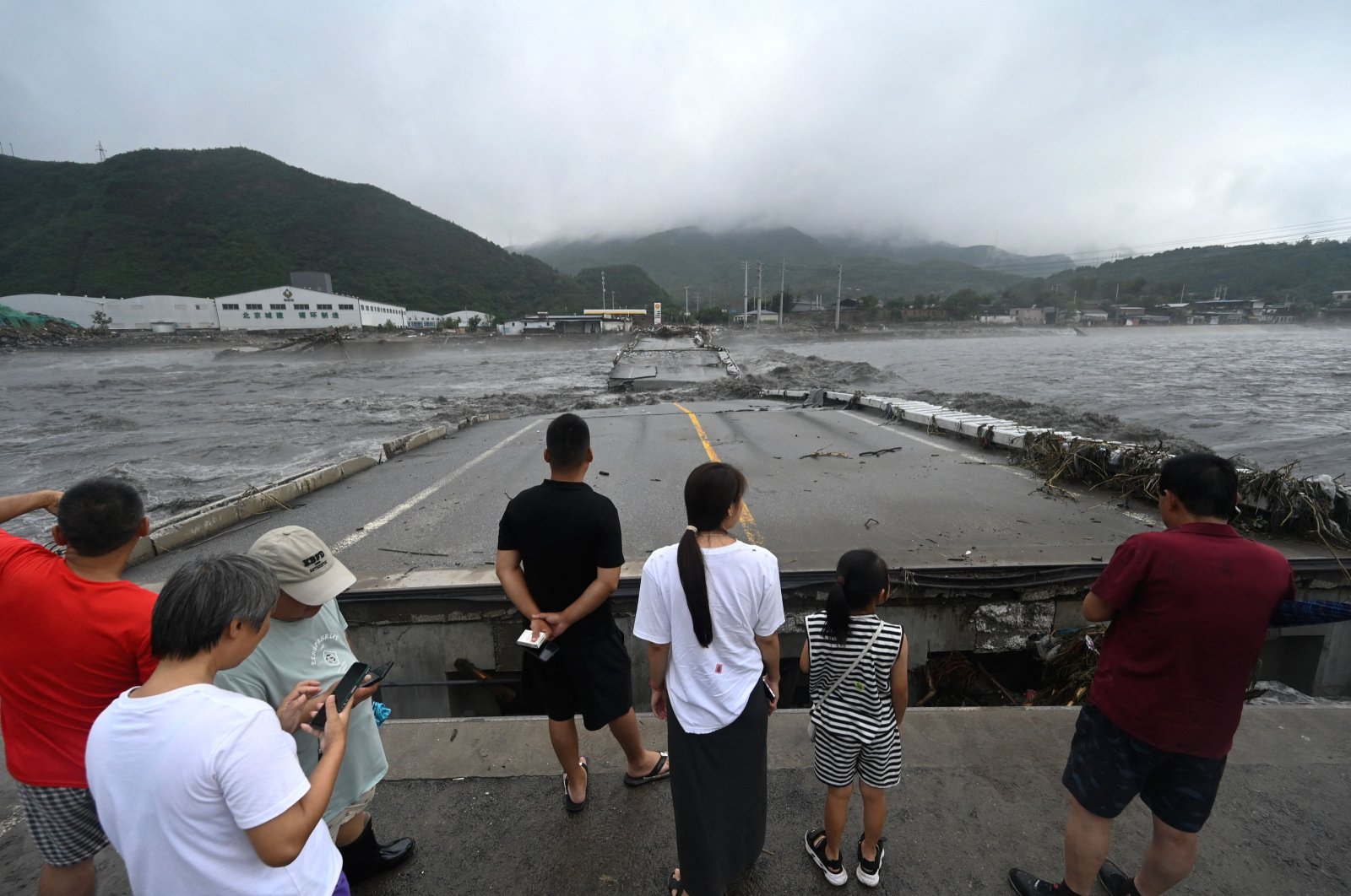 People watch a collapsed bridge on the Dashihe River after heavy rains in Fangshan district in Beijing, China, Aug. 1, 2023. (AFP Photo)