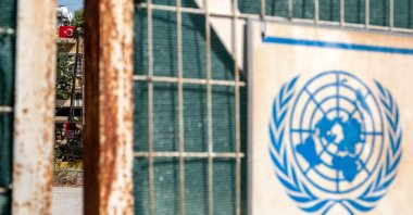 The seal of the United Nations is pictured on a gate leading to the U.N. buffer zone splitting the Cypriot capital Lefkoşa (Nicosia), with a Turkish flag visible in the background in the Turkish Republic of North Cyprus (TRNC), July 11, 2023. (AFP Photo)