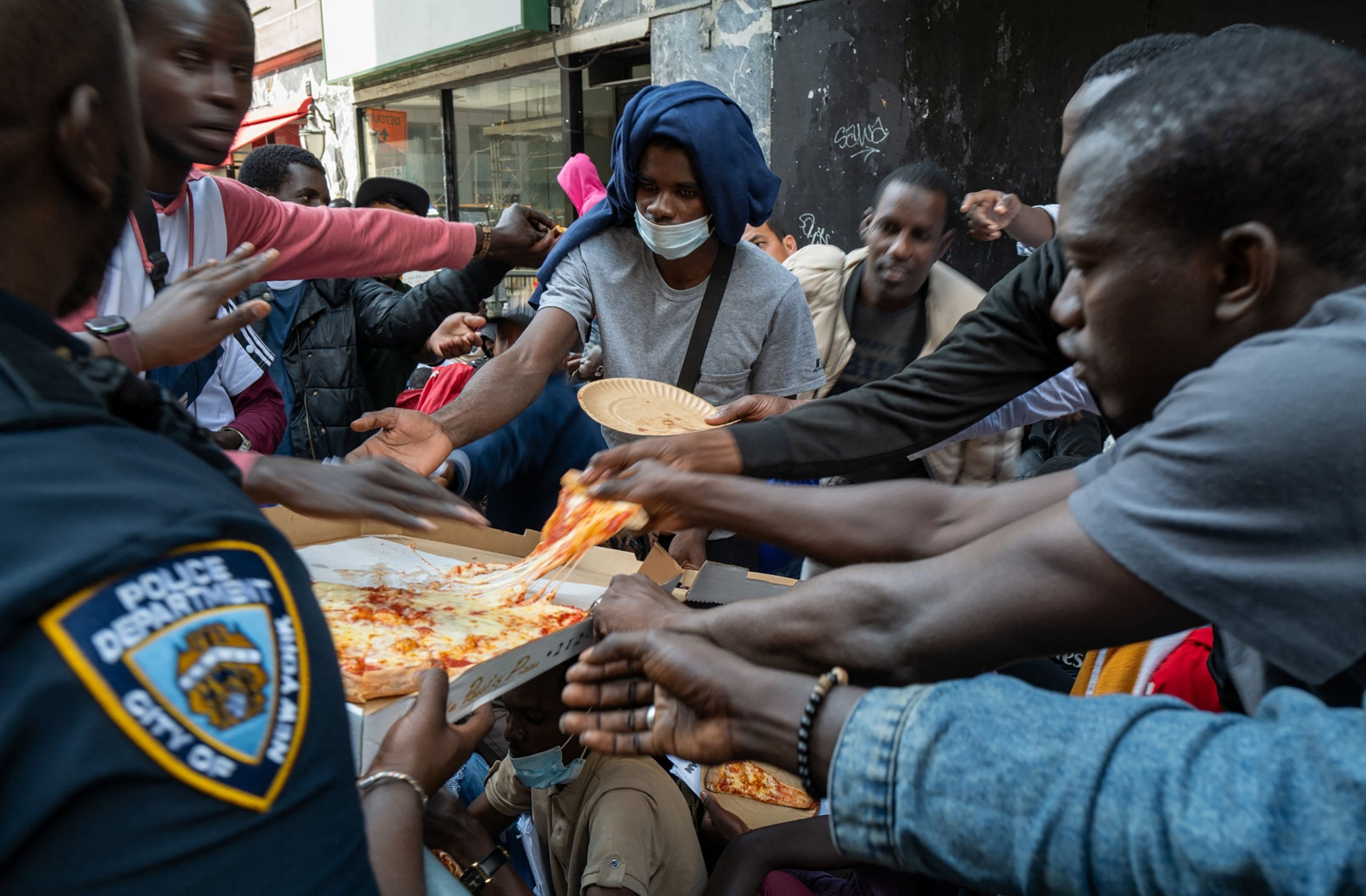 A police officer hands out pizza to dozens of recently arrived migrants to New York City, U.S., Aug. 1, 2023. (AFP Photo)