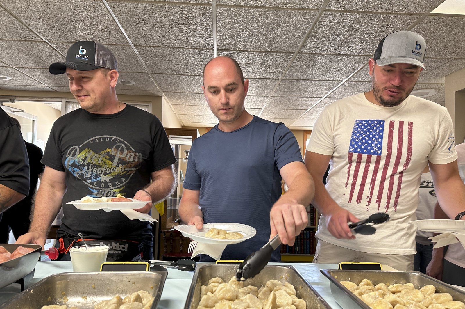 Maksym Bunchukov (L), Andrii Hryshchuk (C) and Ivan Sakivskyi help themselves to perogies at a lunch hosted on July 17, 2023, by the Ukrainian Cultural Institute in Dickinson, North Dakota. (AP Photo)