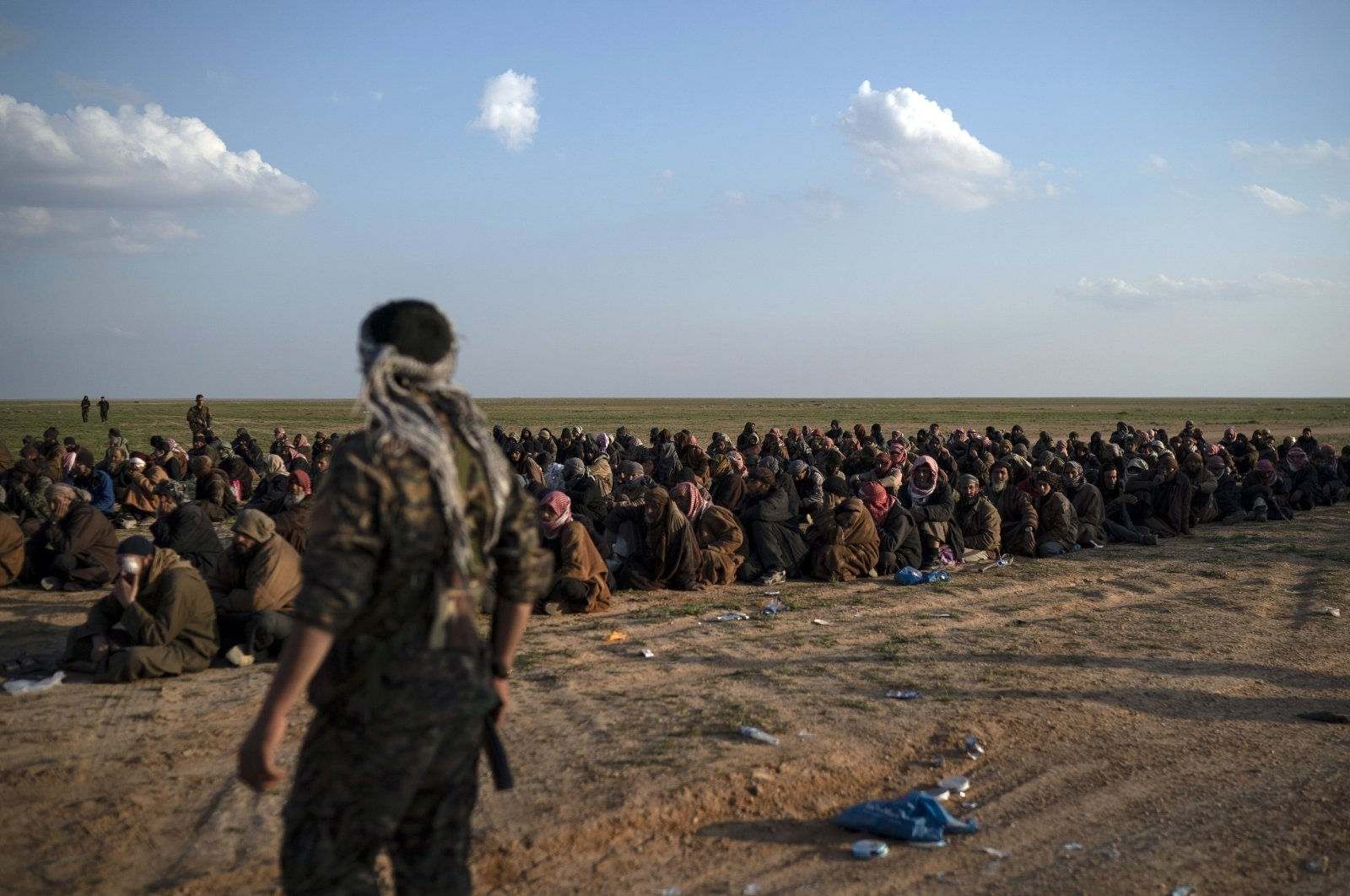 U.S.-backed YPG terrorists stand guard next to men waiting to be screened after being evacuated out of the last territory held by Daesh, near Baghouz, eastern Syria, Feb. 22, 2019. (AP File Photo)
