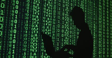 An illustration picture shows a projection of binary code around the shadow of a man holding a laptop computer. (Reuters Photo)