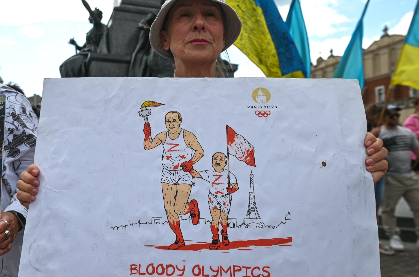 A protester in Krakow holds a poster with Russian President Vladimir Putin and Belarusian President Alexander Lukashenko&#039;s images, featuring an Olympic torch covered in blood and the words "Bloody Olympics," Krakow, Poland, July 23, 2023. (Getty Images Photo)