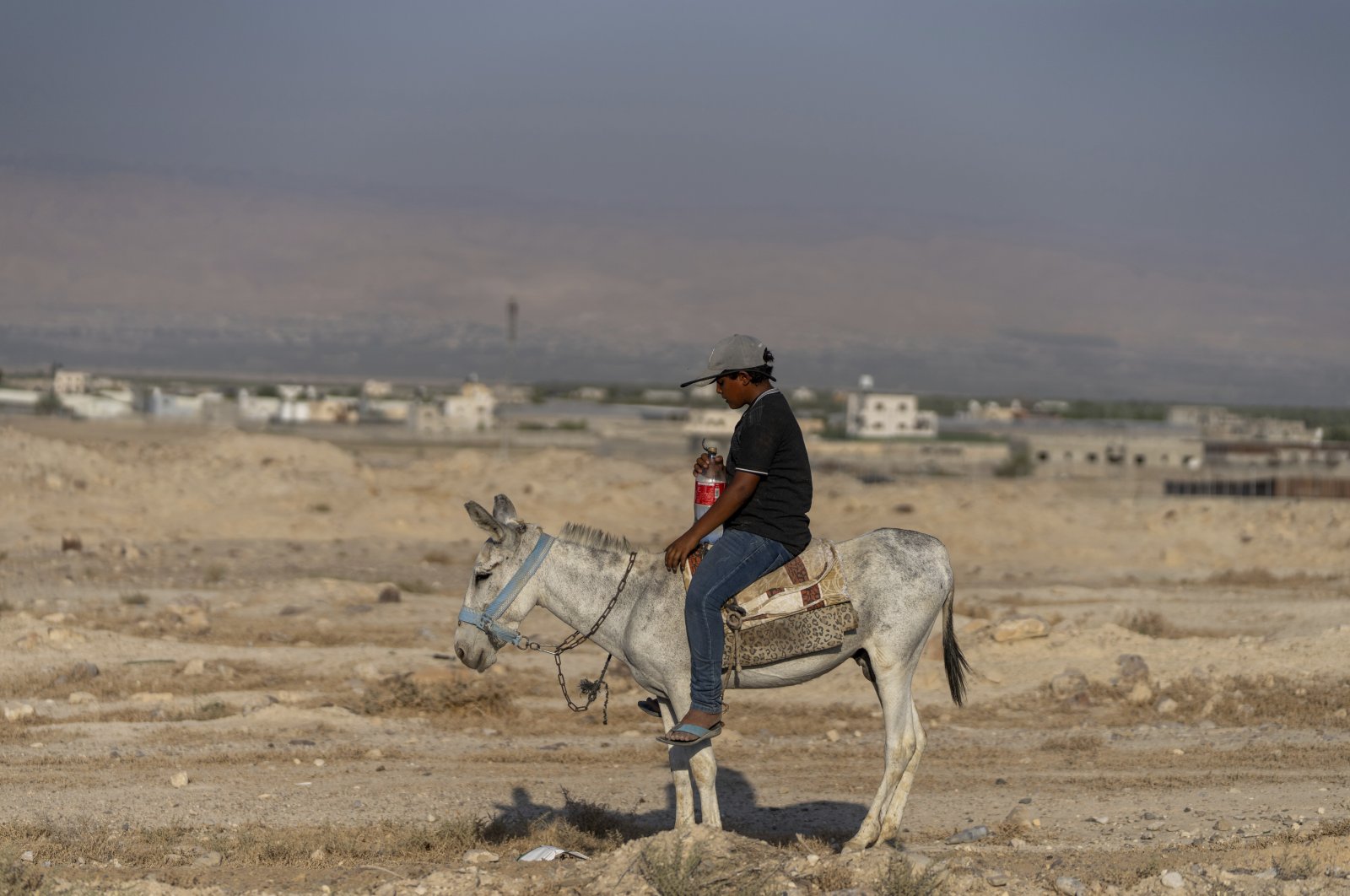 A Palestinian boy rides a donkey through dry land in the northern Jordan Valley, West Bank, Aug. 11, 2023. (AP Photo)