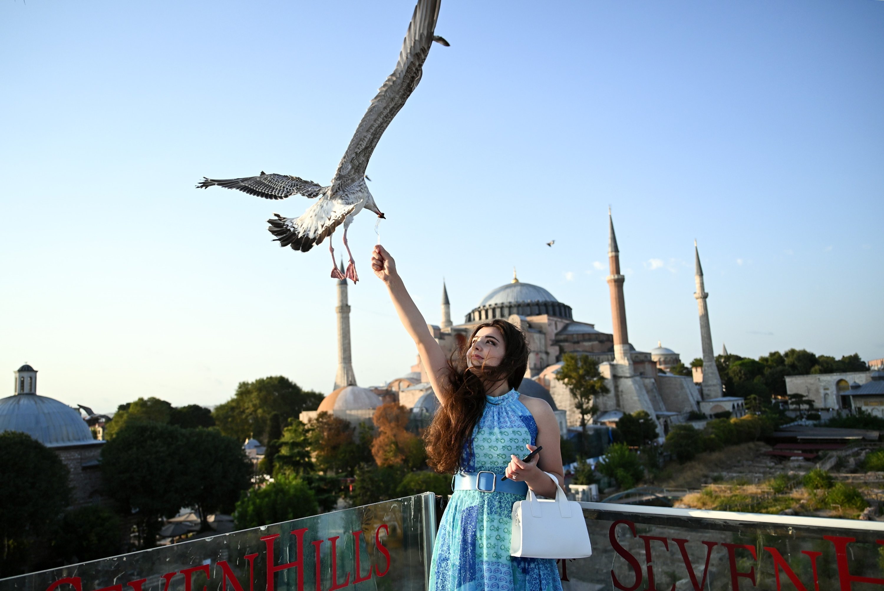 A tourist poses while feeding a seagull in front of the Hagia Sophia Grand Mosque, Istanbul, Türkiye, Aug. 21, 2023. (IHA Photo)