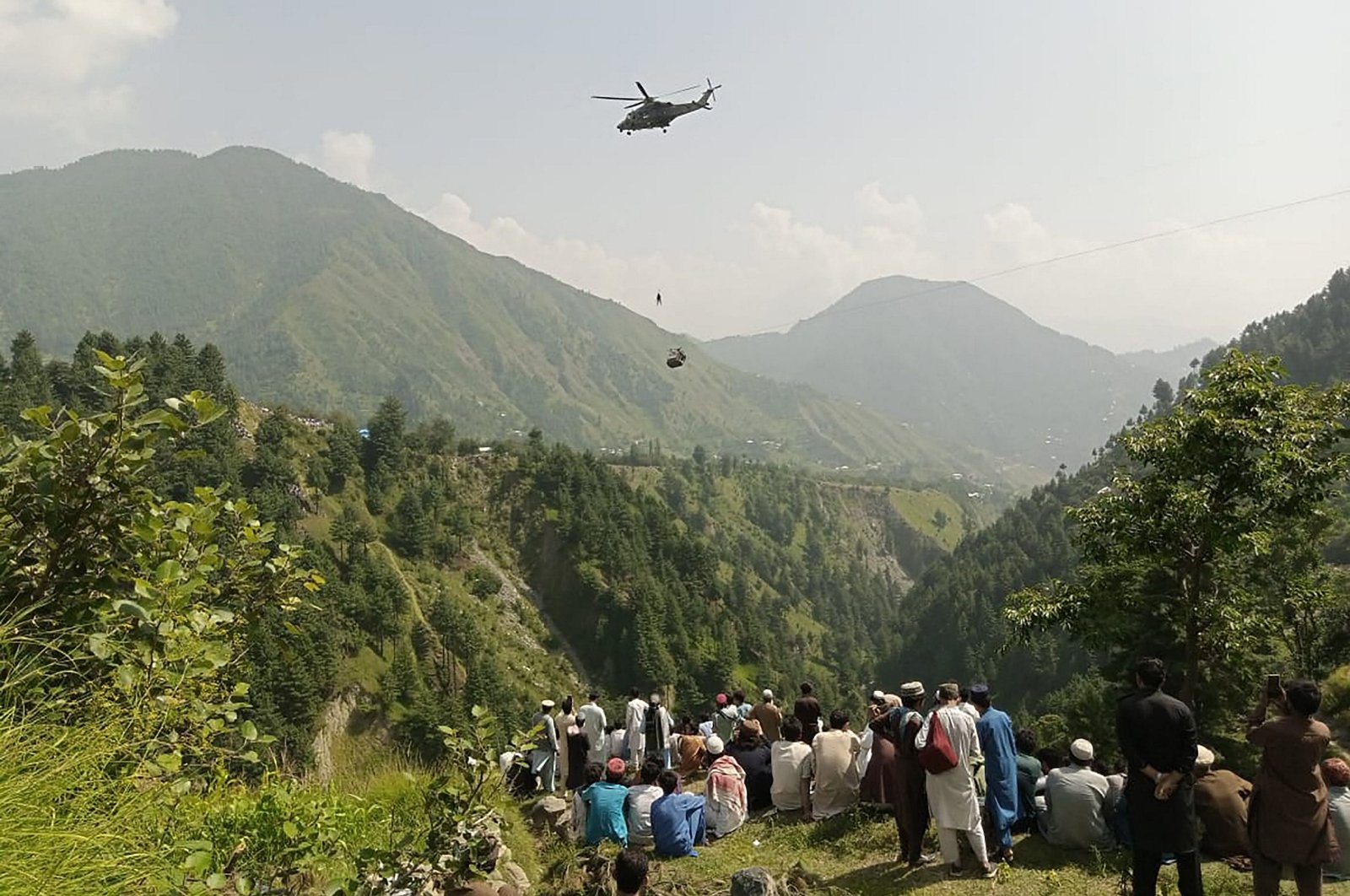 People watch as an army soldier slings down from a helicopter during a rescue mission to recover students stuck in a chairlift in Pashto village, Khyber Pakhtunkhwa province, Aug. 22, 2023. (AFP Photo)