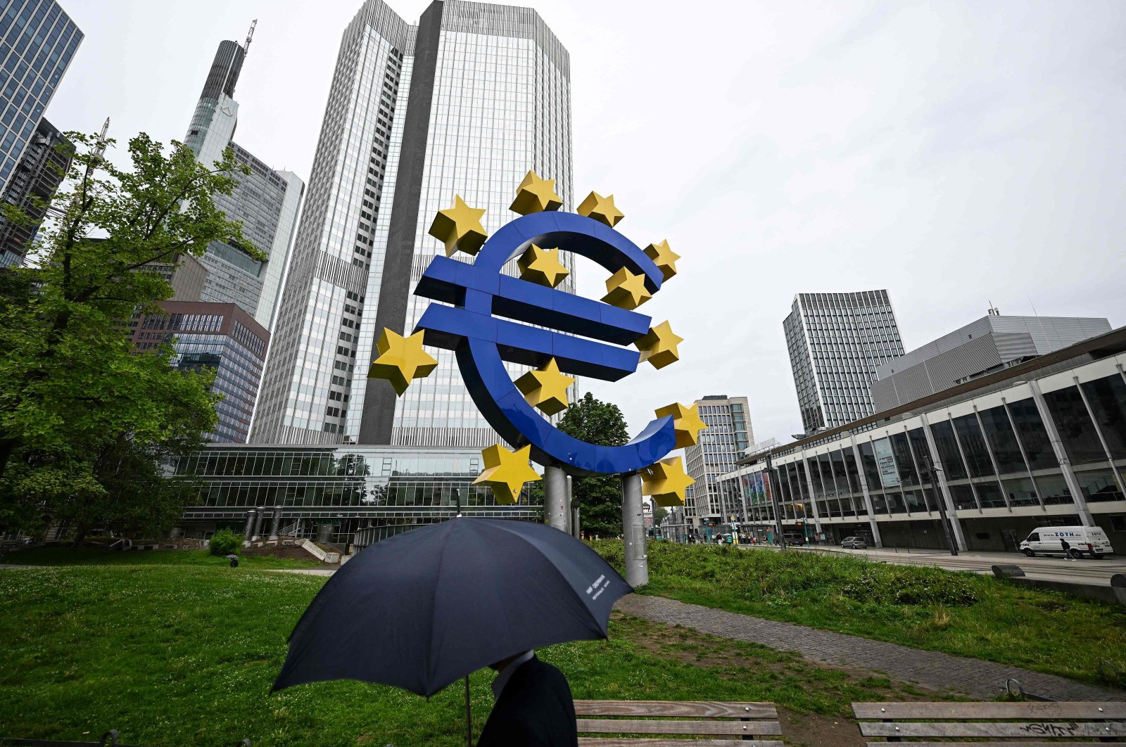 A man with an umbrella walks past the euro currency sign in front of the former European Central Bank (ECB) building, Frankfurt am Main, Germany, July 27, 2023. (AFP Photo)