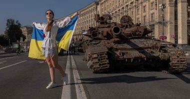 A woman poses for photos holding the Ukrainian flag next to destroyed Russian military vehicles in Kyiv, Ukraine, Aug. 24, 2023. (AFP)