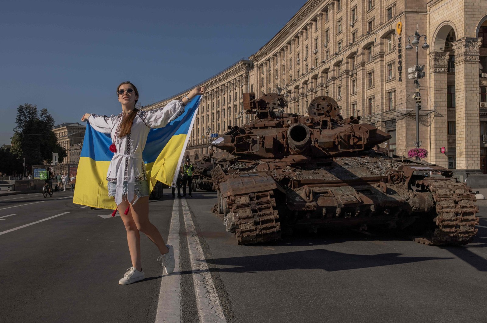 A woman poses for photos holding the Ukrainian flag next to destroyed Russian military vehicles in Kyiv, Ukraine, Aug. 24, 2023. (AFP)