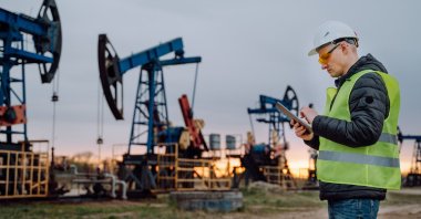 Engineer in protective wear doing a project on digital tablet with the background of oil pumps working in a field at an undisclosed location. (Getty Images Photo)