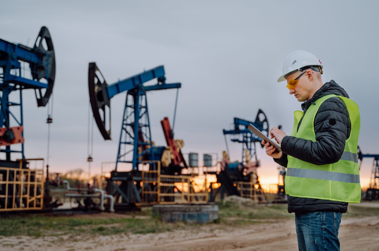 Engineer in protective wear doing a project on digital tablet with the background of oil pumps working in a field at an undisclosed location. (Getty Images Photo)