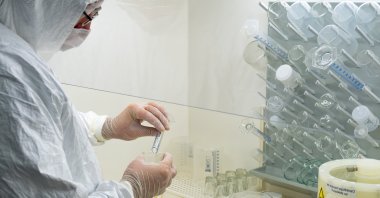 A scientist in a protective white coat, mask and gloves analyzes a virus or bacteria sample in a laboratory with vials, glass flasks and chemicals at an unspecified location in this undated file photo. (Shutterstock File Photo)