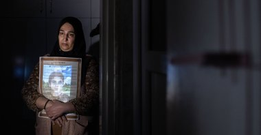 Sariye Tokay embraces a gift her son gave her years ago, as her son's photo is projected on her for a photo exhibition project, in Diyarbakır, southeastern Türkiye, Dec. 9, 2022. (AA Photo)