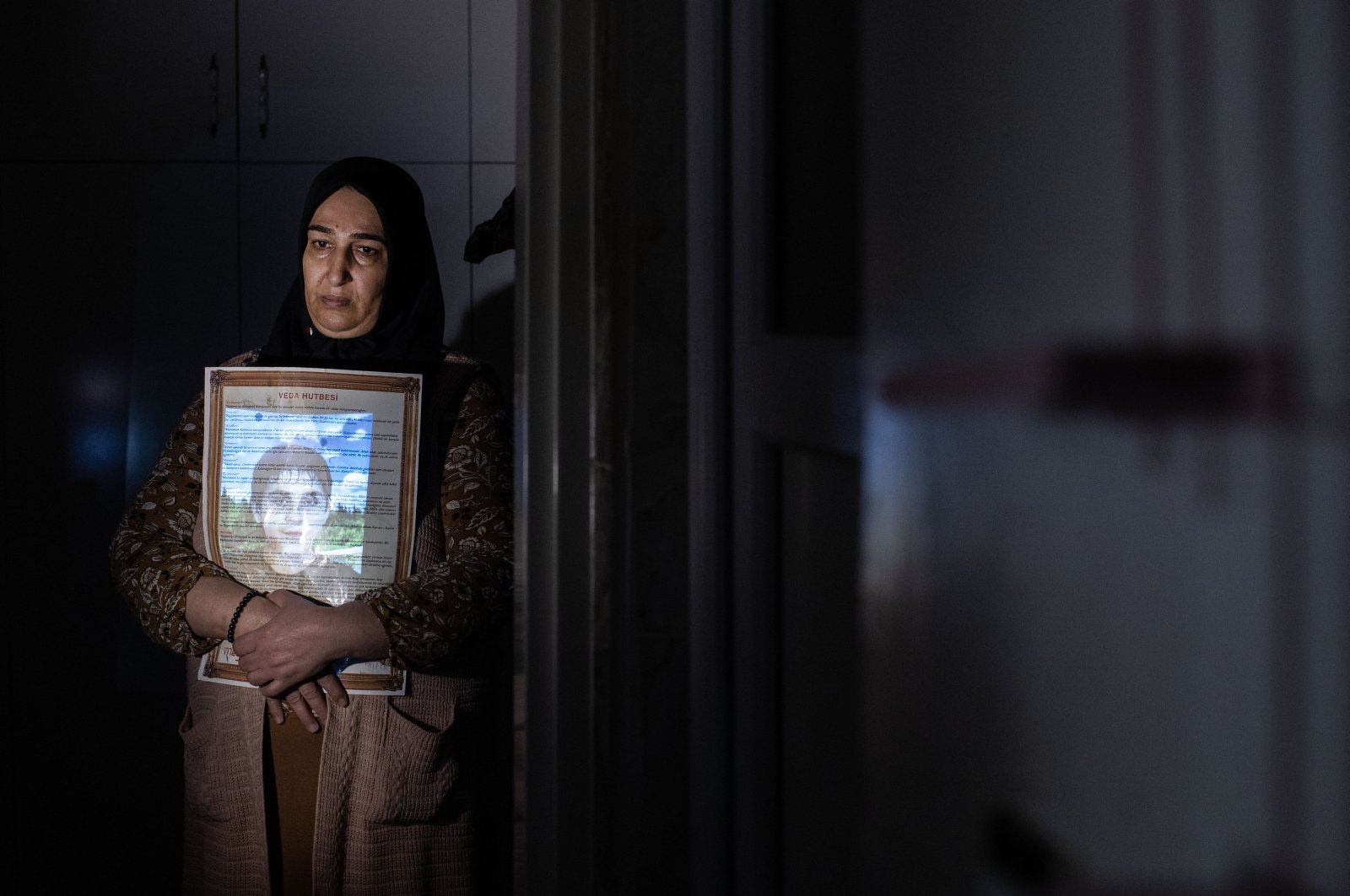 Sariye Tokay embraces a gift her son gave her years ago, as her son&#039;s photo is projected on her for a photo exhibition project, in Diyarbakır, southeastern Türkiye, Dec. 9, 2022. (AA Photo)