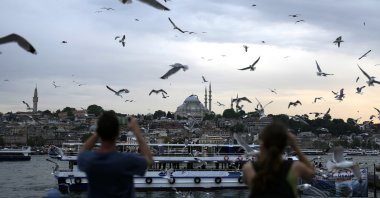 People photograph seagulls as they fly over the Galata Bridge in Istanbul, Türkiye, June 20, 2023.(AP Photo)