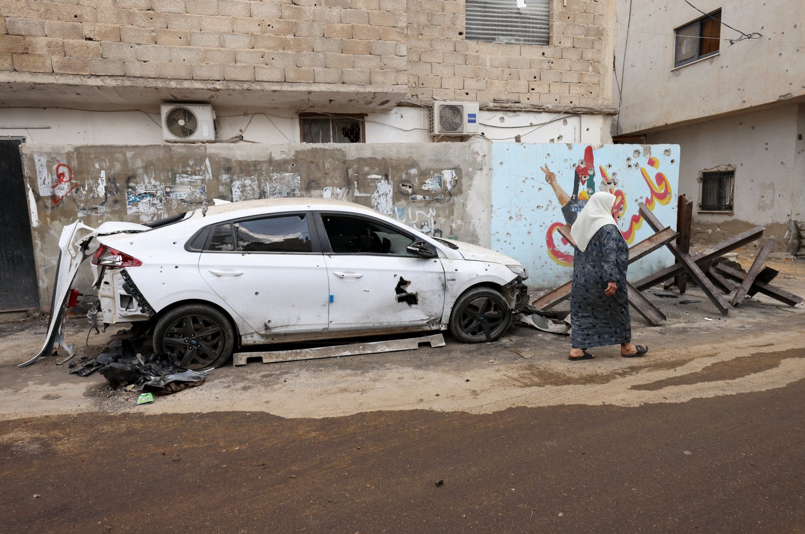 A woman walks past a damaged car following an Israeli military raid at Jenin refugee camp, occupied West Bank, Sept. 20, 2023. (EPA Photo)