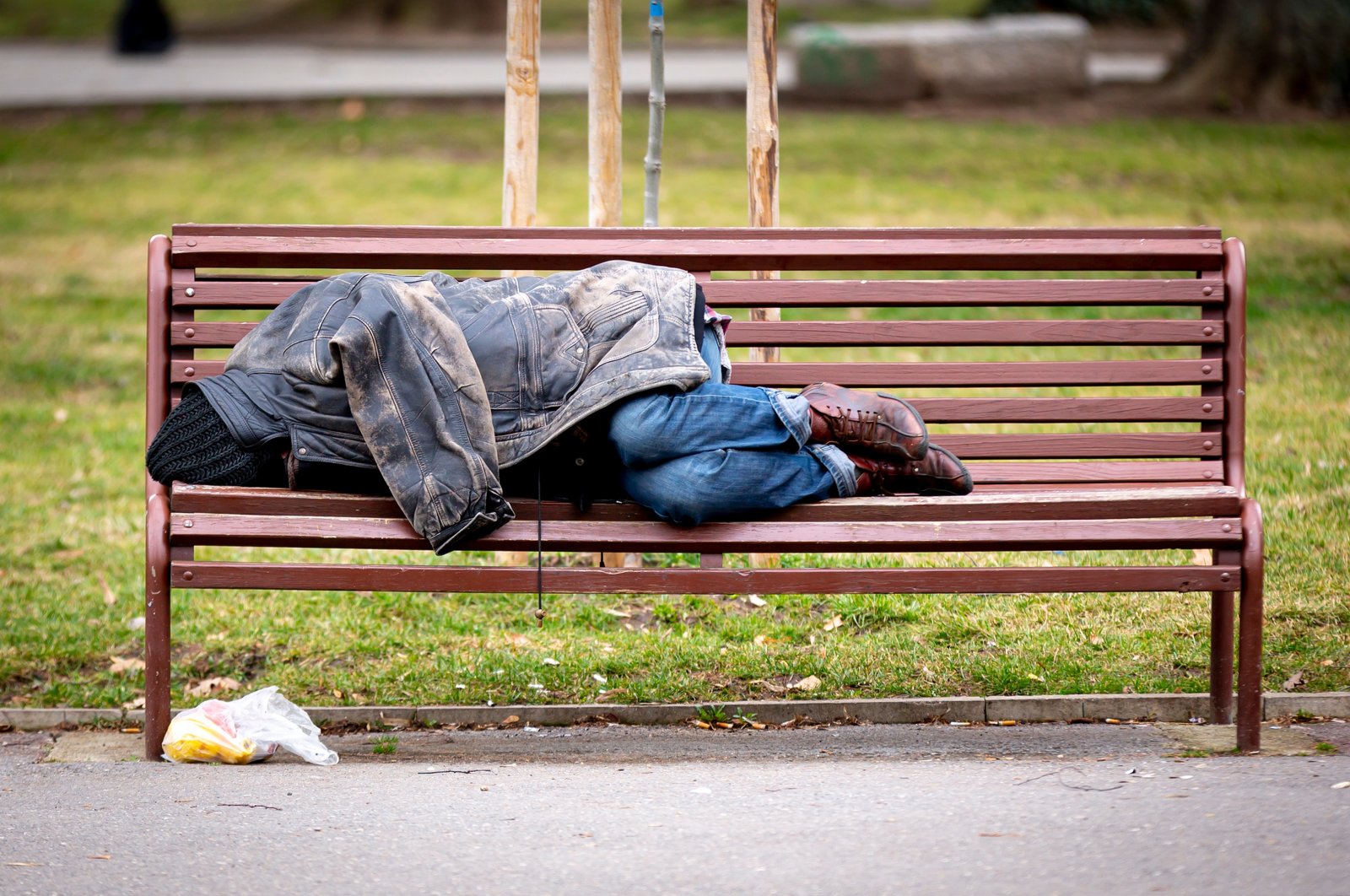 A homeless man sleeps on a bench covered with his jacket in a public park during the day, 2020. (Shutterstcok Photo)