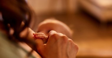 A mother holding her baby&#039;s hand during a breastfeeding, cuddling and sleepy moment. (Shutterstock Photo)