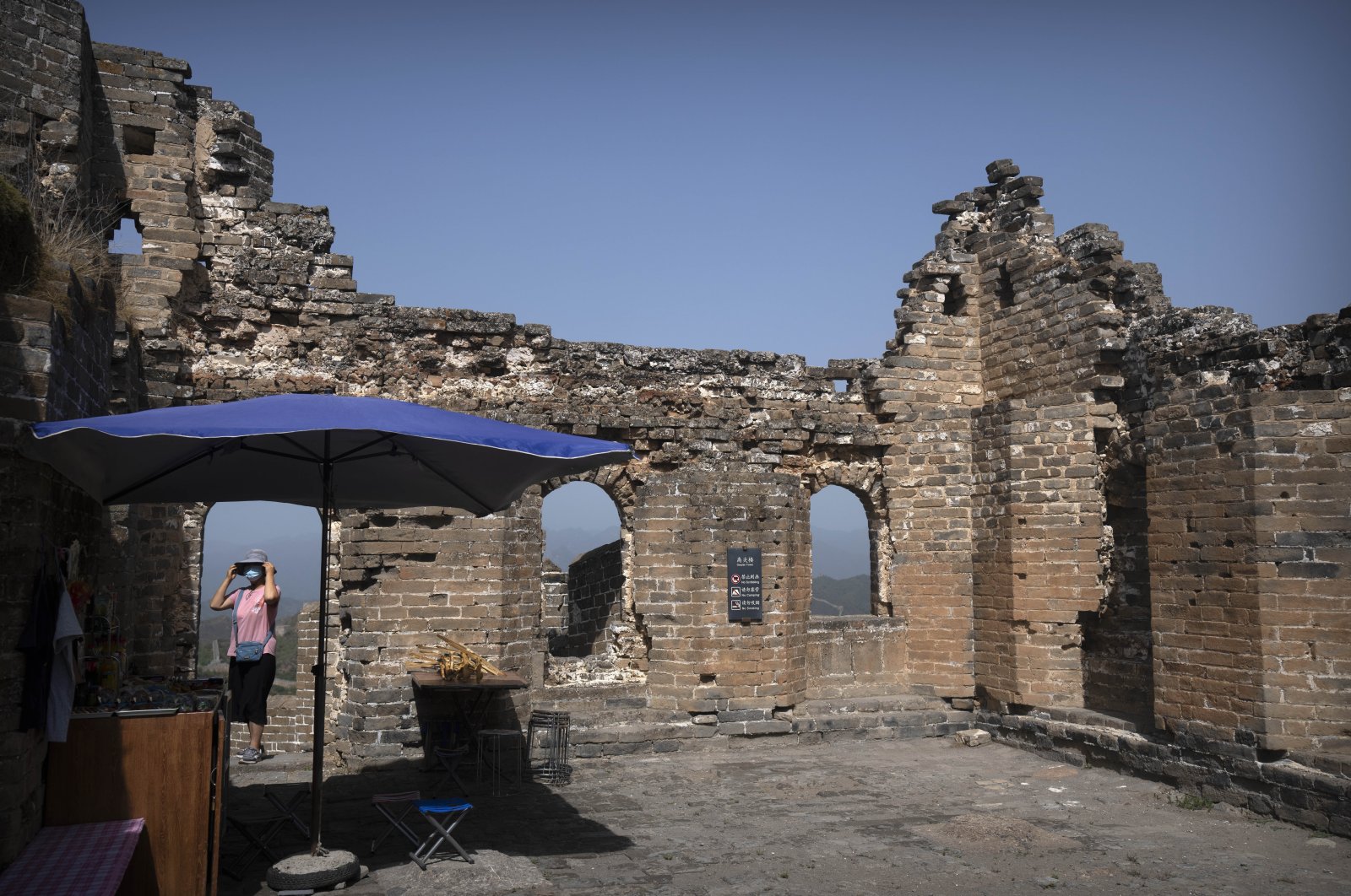 A vendor adjusts her hat as she waits for visitors to arrive at her refreshment stand in a tower on the Jinshanling section of the Great Wall of China in northern China&#039;s Hebei Province, July 5, 2023. (AP Photo)