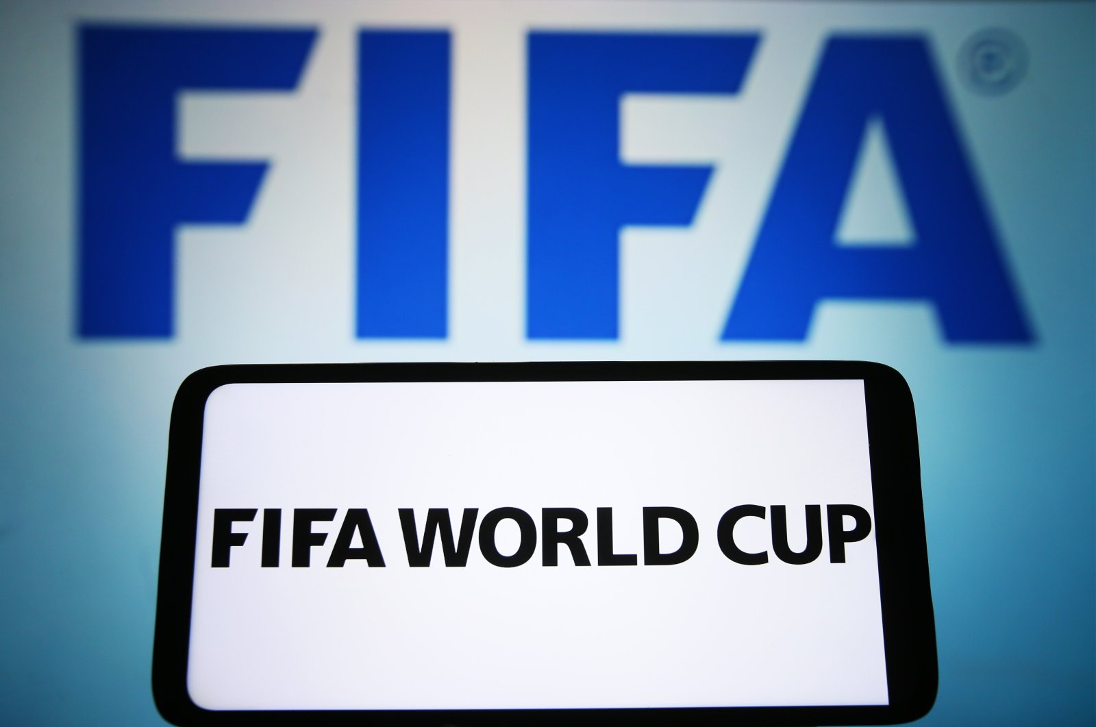 FIFA World Cup words are seen displayed on a smartphone and FIFA logo on the background, March 17, 2023. (Getty Images File Photo)