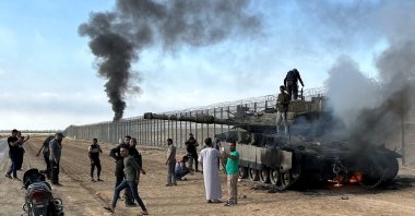 Palestinians react as an Israeli military vehicle burns at the Israeli side of the Israel-Gaza border, Oct. 7, 2023. (Reuters Photo)