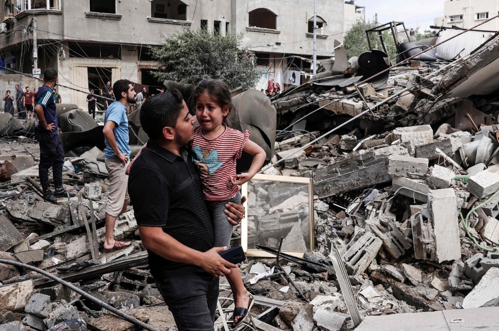 A man carries a crying child as he walks in front of a building destroyed in an Israeli air strike in Gaza City on Oct. 7, 2023. (AFP Photo)