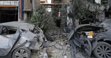 A Palestinian woman stands at the gate of a damaged building behind destroyed cars following Israeli airstrikes, Gaza City, Palestine, Oct. 10, 2023. (AFP Photo)