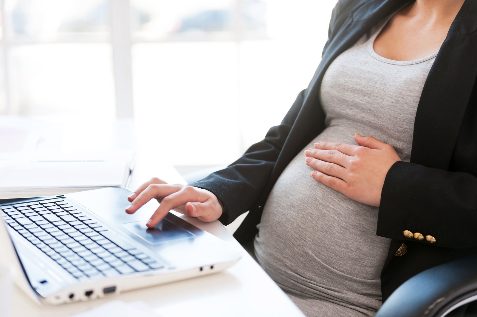 A pregnant woman works on a laptop while sitting at her workplace in an office. (Shutterstock Photo)