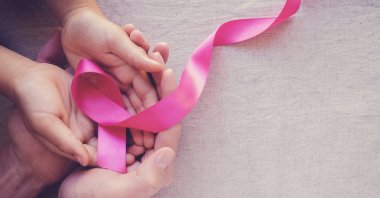 Adult and child hands are seen holding a pink ribbon symbolizing breast cancer awareness. (Shutterstock Photo)