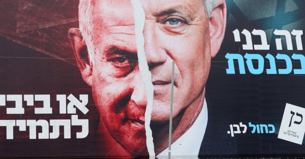 A boy looks up at a Blue and White party election campaign banner depicting its leader, former Israeli Defense Minister Benny Gantz, alongside Israeli Prime Minister Benjamin Netanyahu, ahead of the March 23 ballot, Bnei Brak, Israel March 22, 2021. (Reuters File Photo)