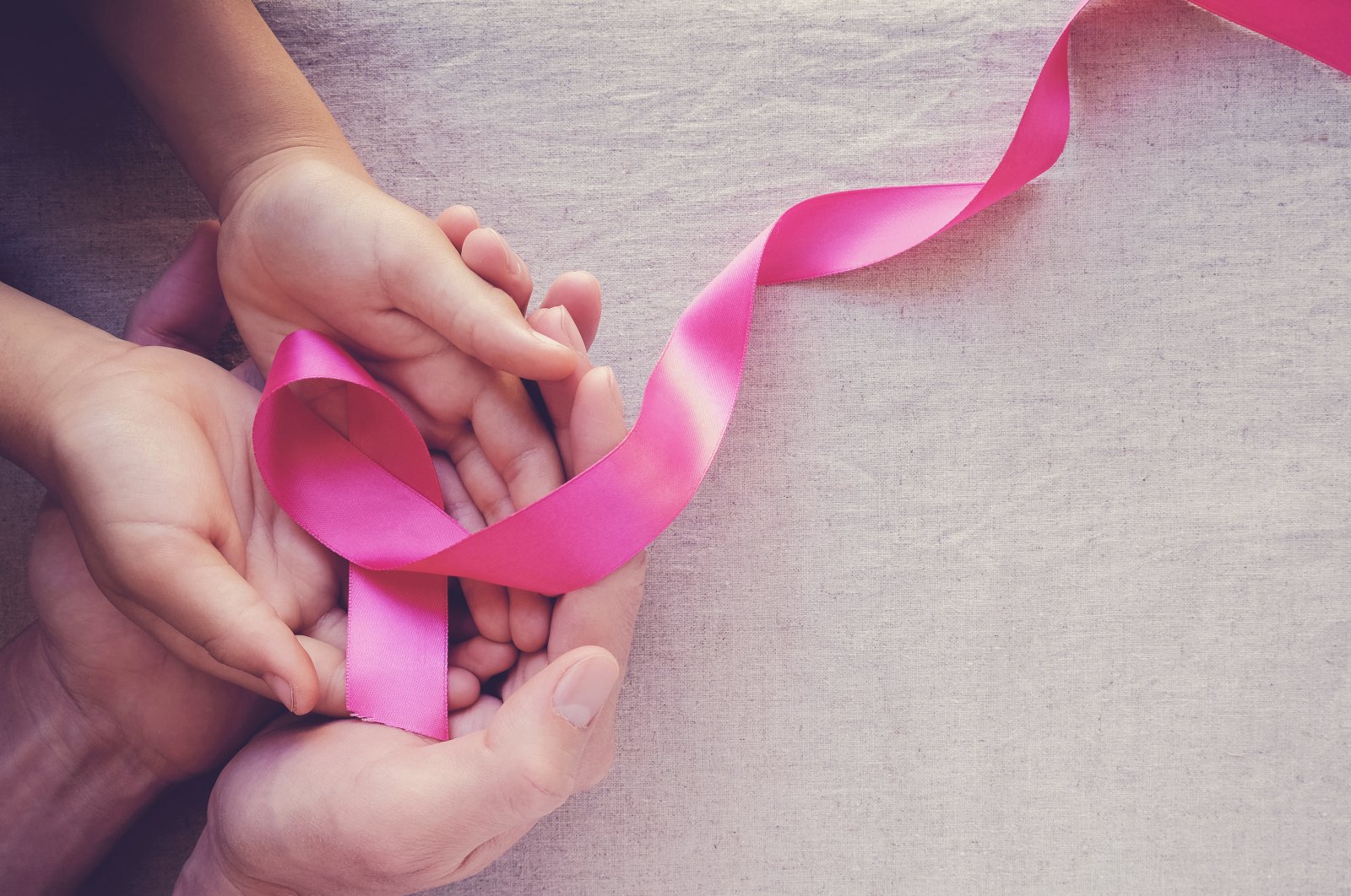 Adult and child hands are seen holding a pink ribbon symbolizing breast cancer awareness. (Shutterstock Photo)